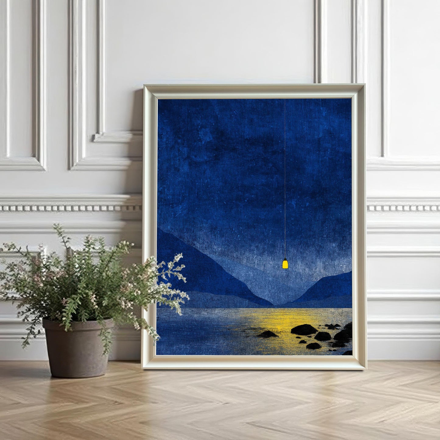 White wood framed blue mountain print leaning against a white decorative wall next to a potted plant on a herringbone wood floor.