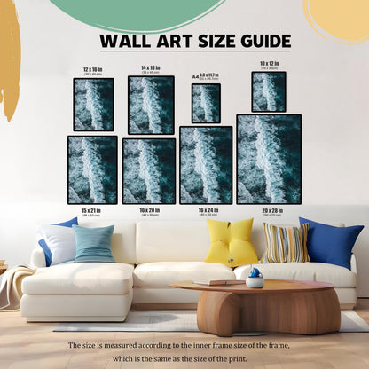 Wall art size guide showing different framed print sizes (e.g., 12×16 in, 16×24 in, 20×28 in) displayed above a white sectional sofa, helping customers visualize the scale of the dark blue ocean wave print in a living room setting.