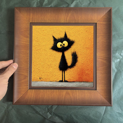 Front view of a square wood-framed print of a quirky black cat illustration, held against a dark green textured background to showcase frame detail.