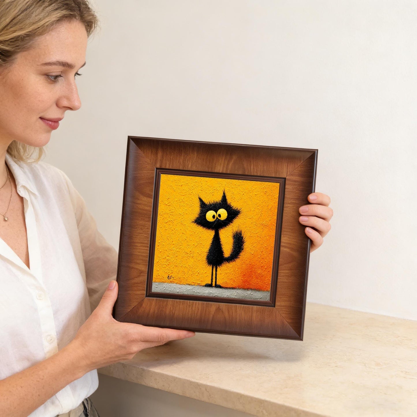 A woman holding a square dark wood-framed art piece featuring a fuzzy black cat, demonstrating the scale and quality of the handmade decor.