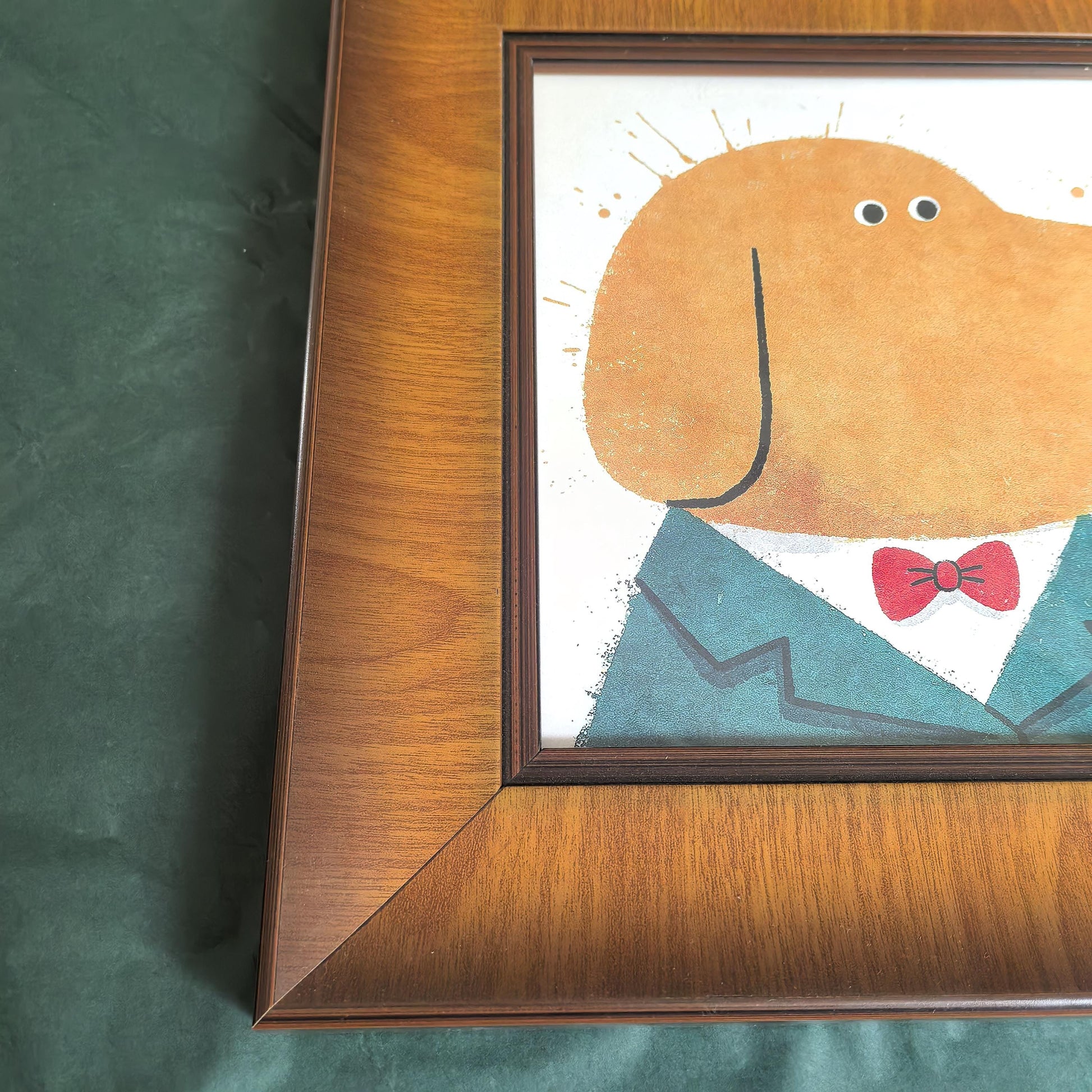 A high-resolution close-up showing the corner detail of a wide, dark wood picture frame with a rich grain finish, framing a colorful dog art print.