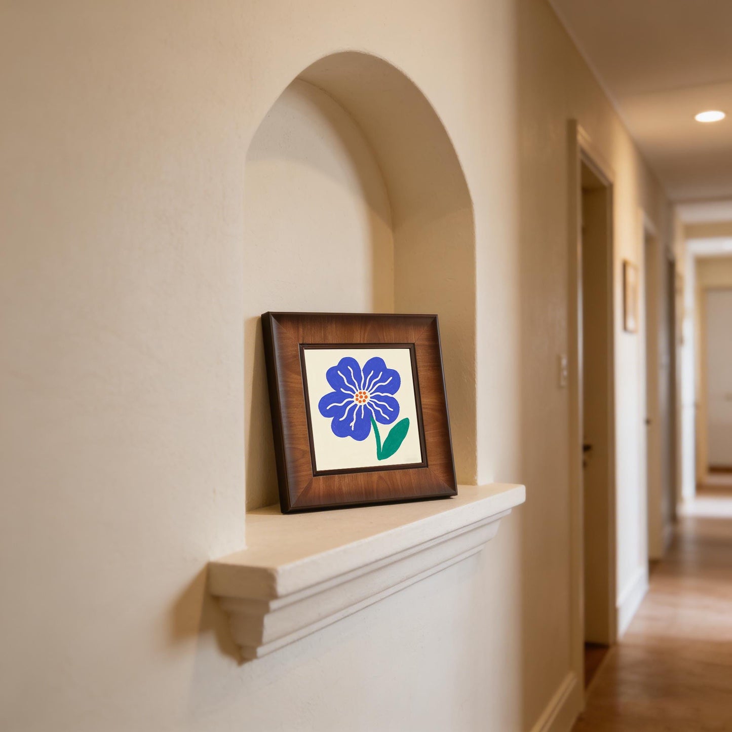 Minimalist blue flower art print in a brown wooden frame displayed inside a modern arched wall niche in a brightly lit hallway.