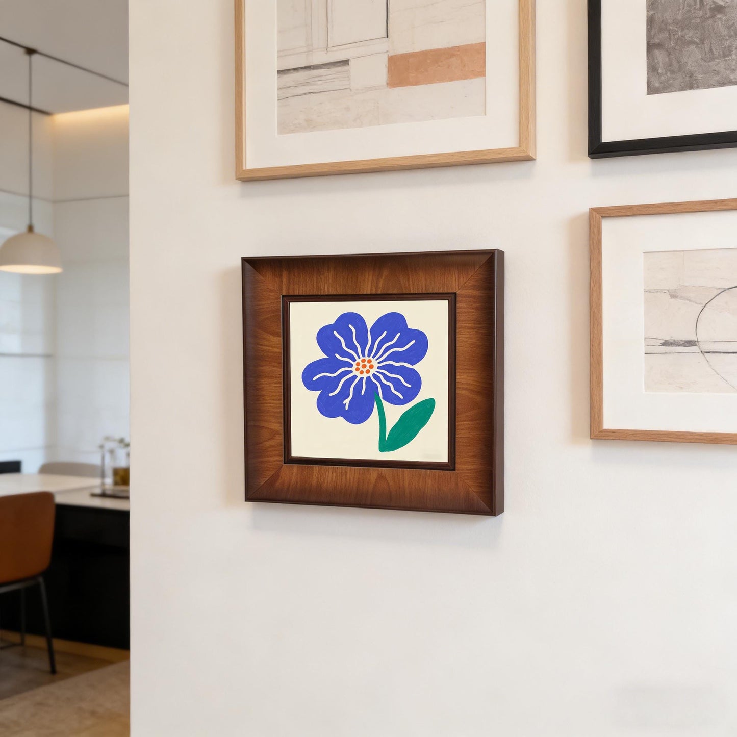 Square dark wood-framed flower print hanging on a white gallery wall alongside other modern minimalist art pieces in a contemporary home.