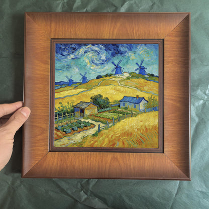 A person’s hand holding a square wooden frame against a green background, providing a clear sense of the product's physical scale and depth.