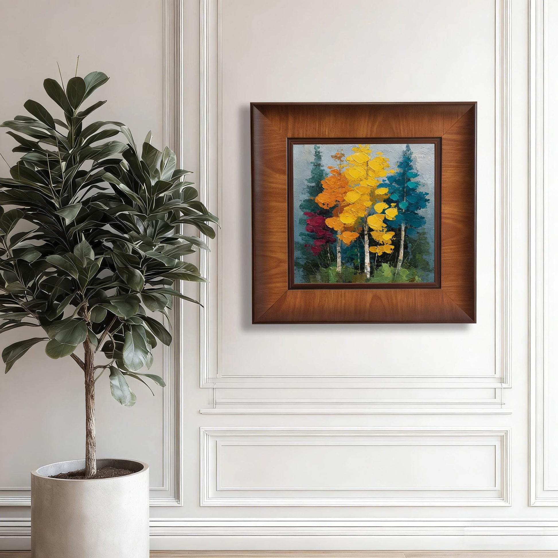 Square walnut-framed landscape art hanging on a white paneled wall next to a tall fiddle leaf fig plant in a white pot.