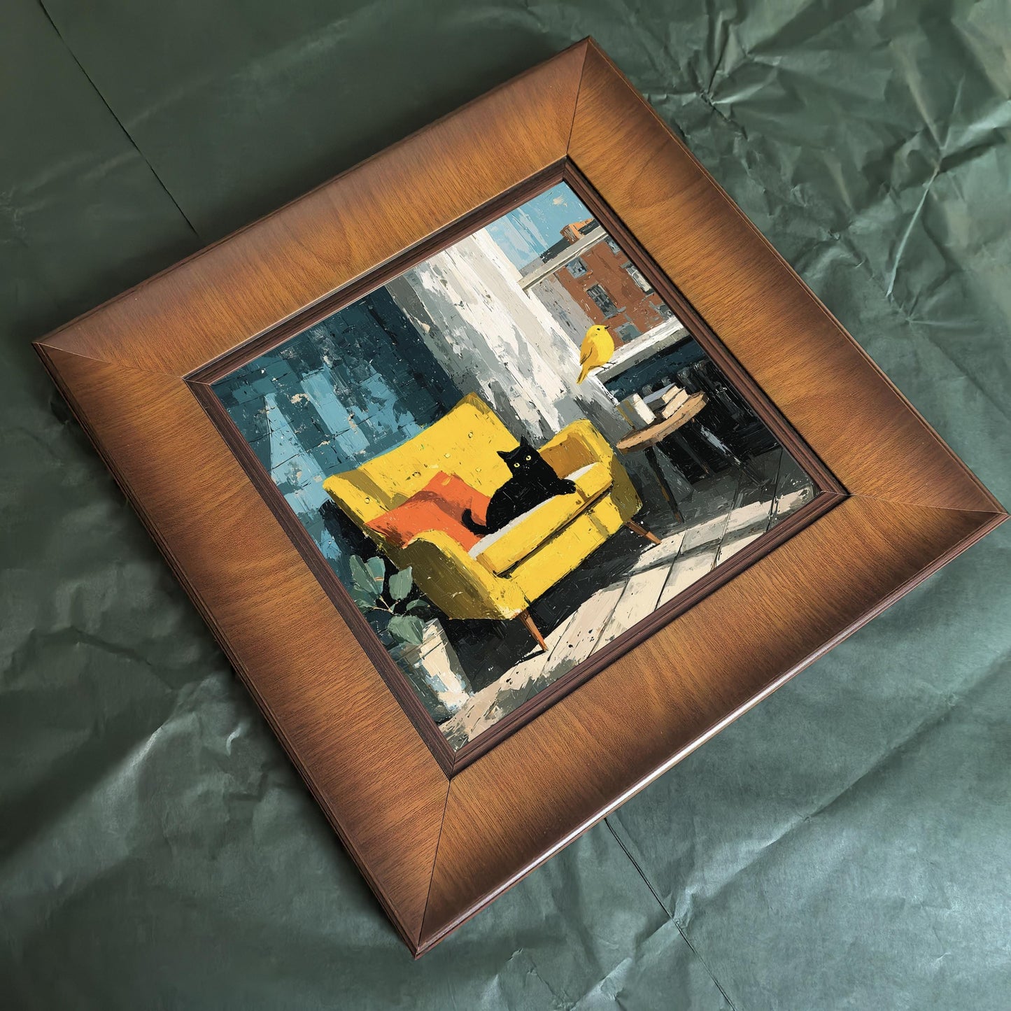 An overhead flat-lay view of a square wood-framed art print resting on a textured dark green background.