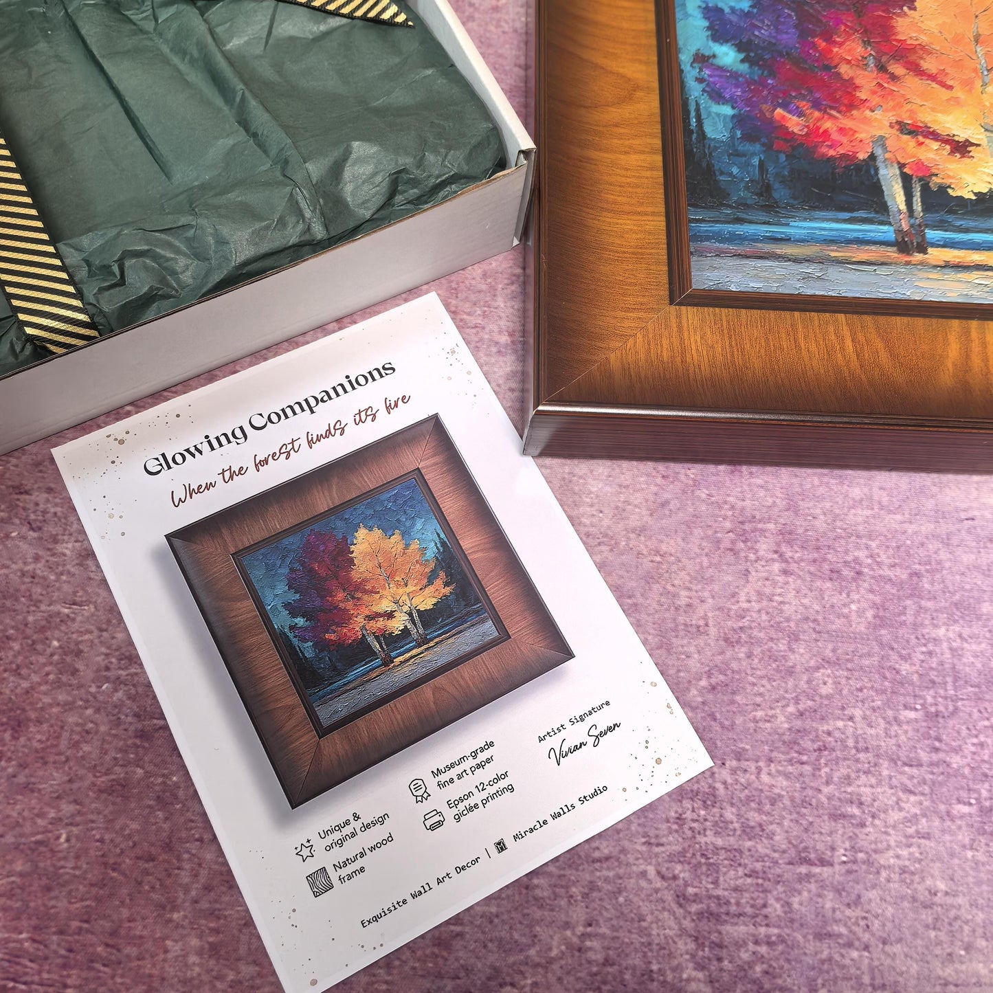 A square, dark wood-framed art print titled "Glowing Companions" is displayed next to an open "Miracle Walls" gift box. The box is lined with dark green tissue paper and tied with a gold-striped ribbon, while a product information card is placed in the foreground.