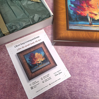 A square, dark wood-framed art print titled "Glowing Companions" is displayed next to an open "Miracle Walls" gift box. The box is lined with dark green tissue paper and tied with a gold-striped ribbon, while a product information card is placed in the foreground.