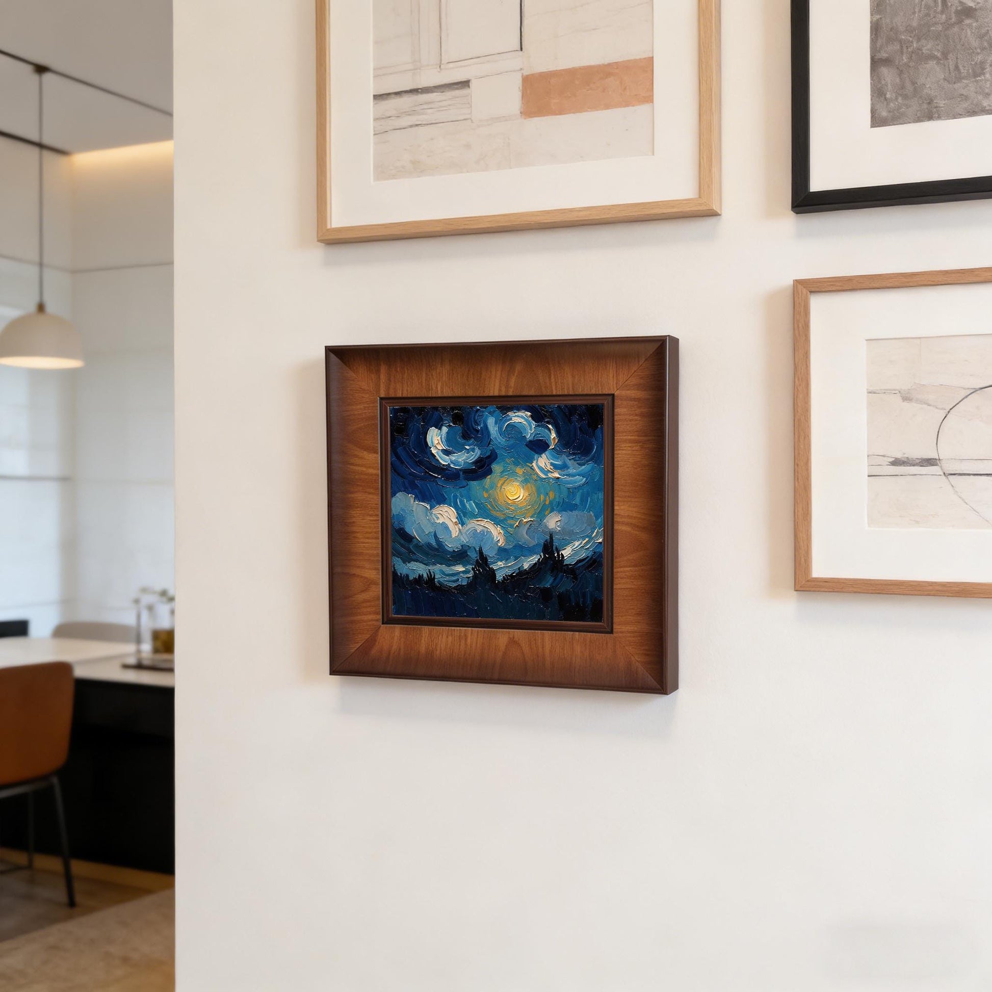 Close-up of a square wooden framed wall art piece hanging as part of a gallery wall set in a modern, bright dining area with minimalist furniture.