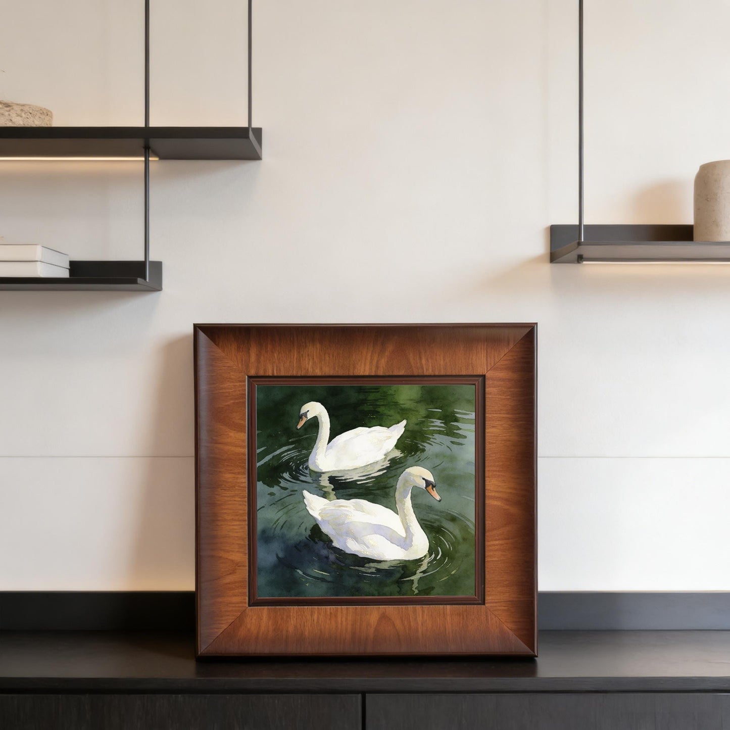 Square framed swan artwork displayed on a black sideboard or shelf against a clean white wall in a contemporary home interior.