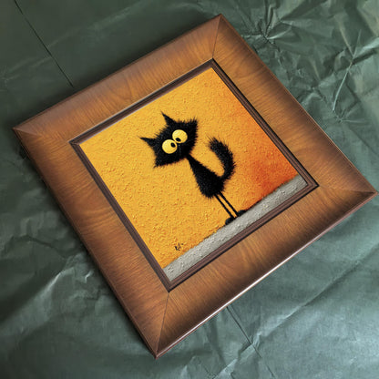 Overhead angled shot of a square wooden frame featuring a textured black cat painting, lying on a green paper background to highlight the wood grain.
