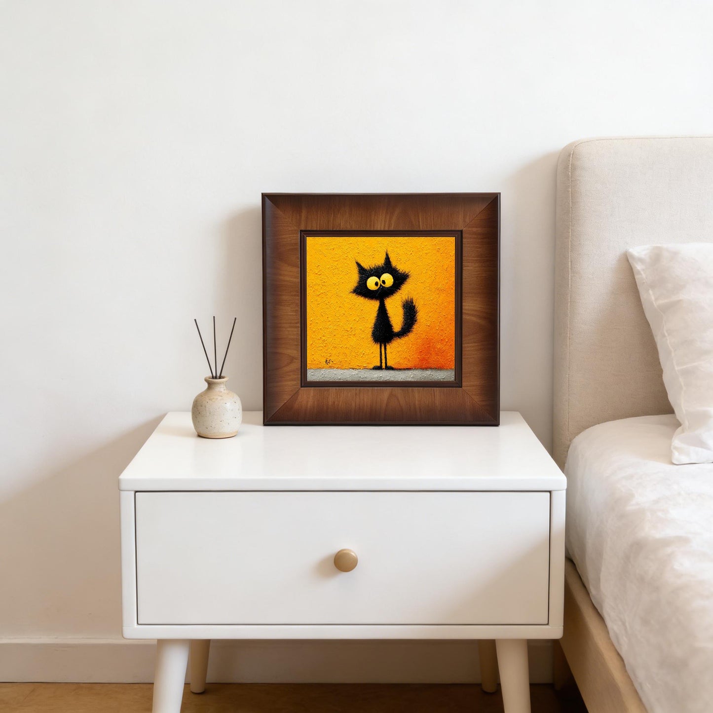 Square framed quirky cat wall art displayed on a white minimalist nightstand next to a bed, creating a cozy and modern bedroom decor aesthetic.