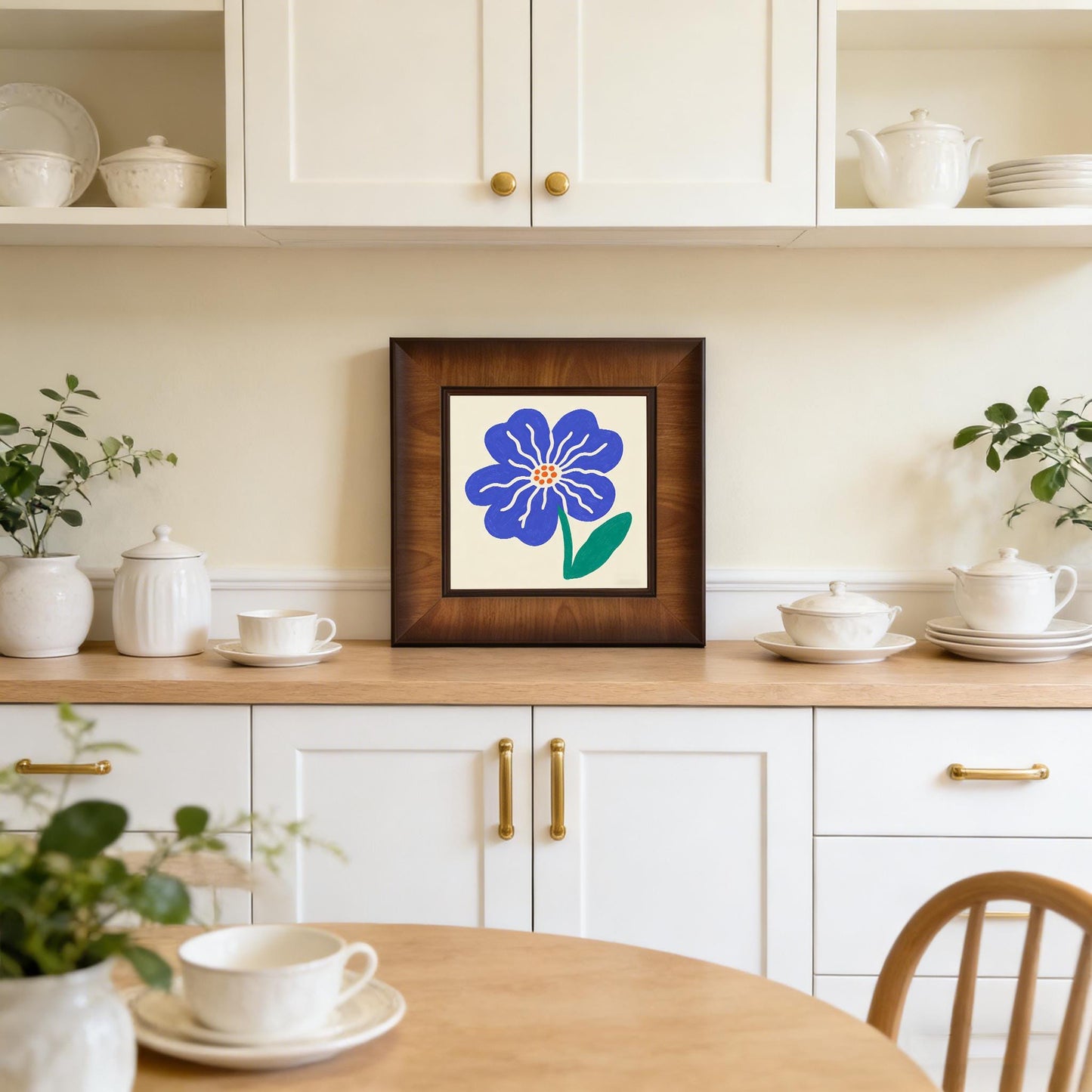 Blue floral framed print styled as kitchen decor, sitting on a wooden countertop among white ceramic jars and teacups.