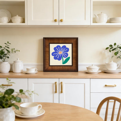 Blue floral framed print styled as kitchen decor, sitting on a wooden countertop among white ceramic jars and teacups.