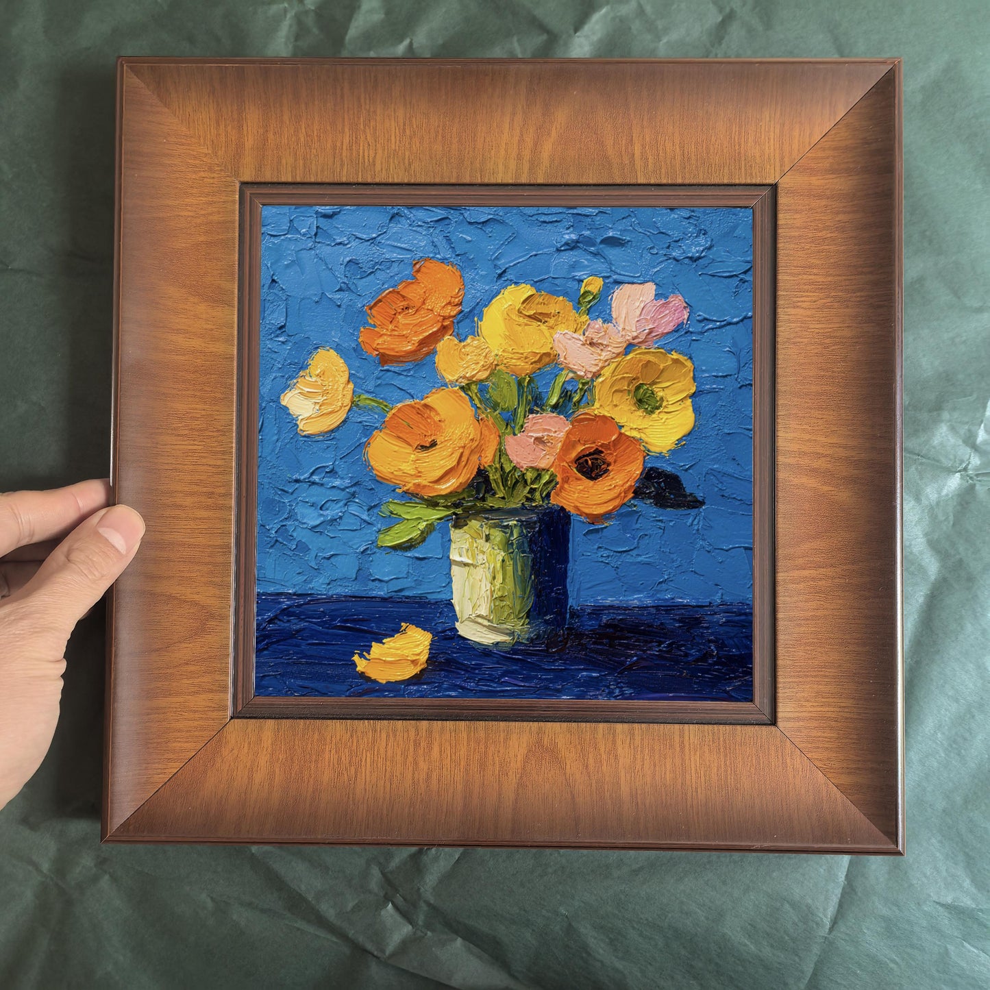 Top-down view of a square wood-framed floral painting with thick impasto texture, featuring yellow poppies against a bright blue background.