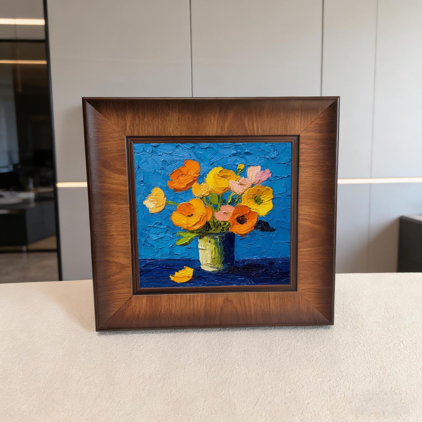 Square wood-framed textured flower painting displayed on a white console table in a minimalist, high-end room setting.