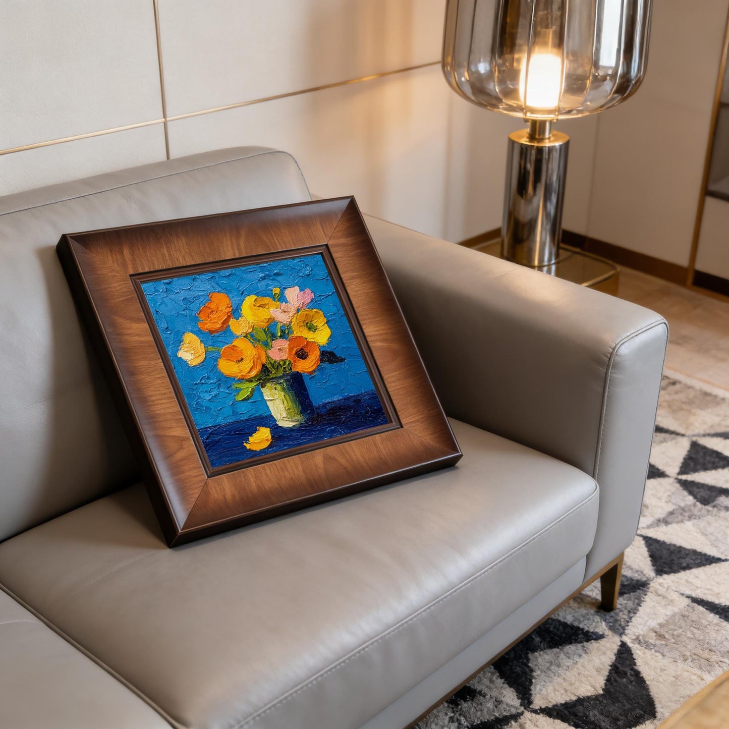 Square floral wall art in a dark wood frame displayed on a modern grey leather sofa next to a stylish glass floor lamp.