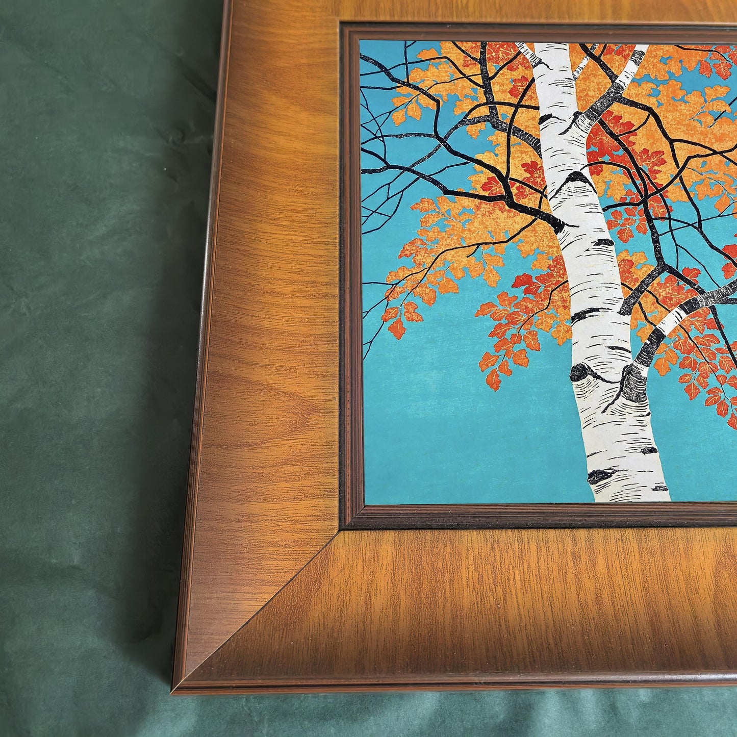 Close-up of a wide wood picture frame featuring a vibrant birch tree illustration with orange autumn leaves on a teal background.