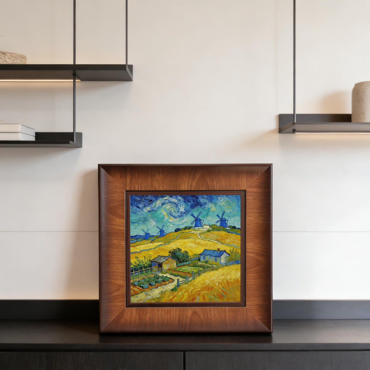 A square-framed impressionist painting of a golden wheat field and windmills displayed on a black modern sideboard under sleek pendant lighting.