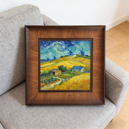 A square wood-framed painting of blue windmills and yellow fields resting on a grey fabric sofa, demonstrating how the art looks in a casual living space.