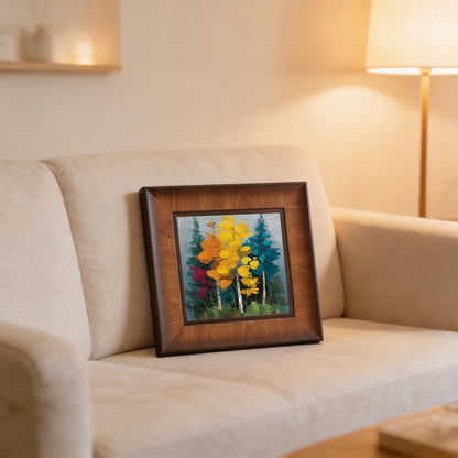 A textured forest art print in a deep brown wooden frame, leaning against the back of a beige fabric sofa in a cozy, warm-lit living room.