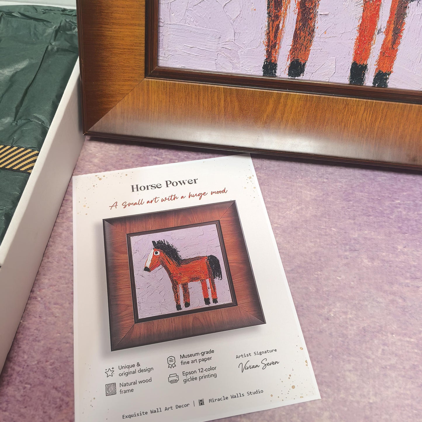 A close-up shot of the "Horse Power" product card resting in front of the framed artwork. The card features the slogan "A small art with a huge mood" and lists quality details like natural wood frame and 12-color giclée printing.