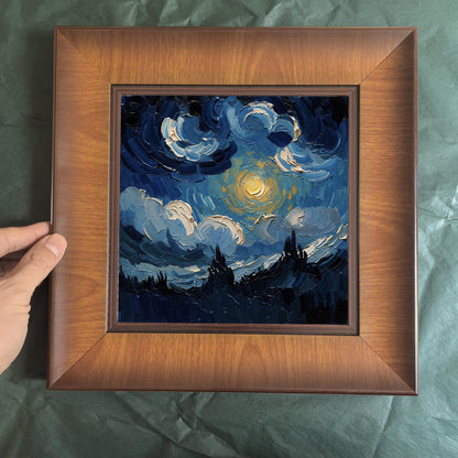 A person's hand holding the side of a square dark wood frame containing a thick-textured blue painting of clouds and a bright moon over a dark landscape.