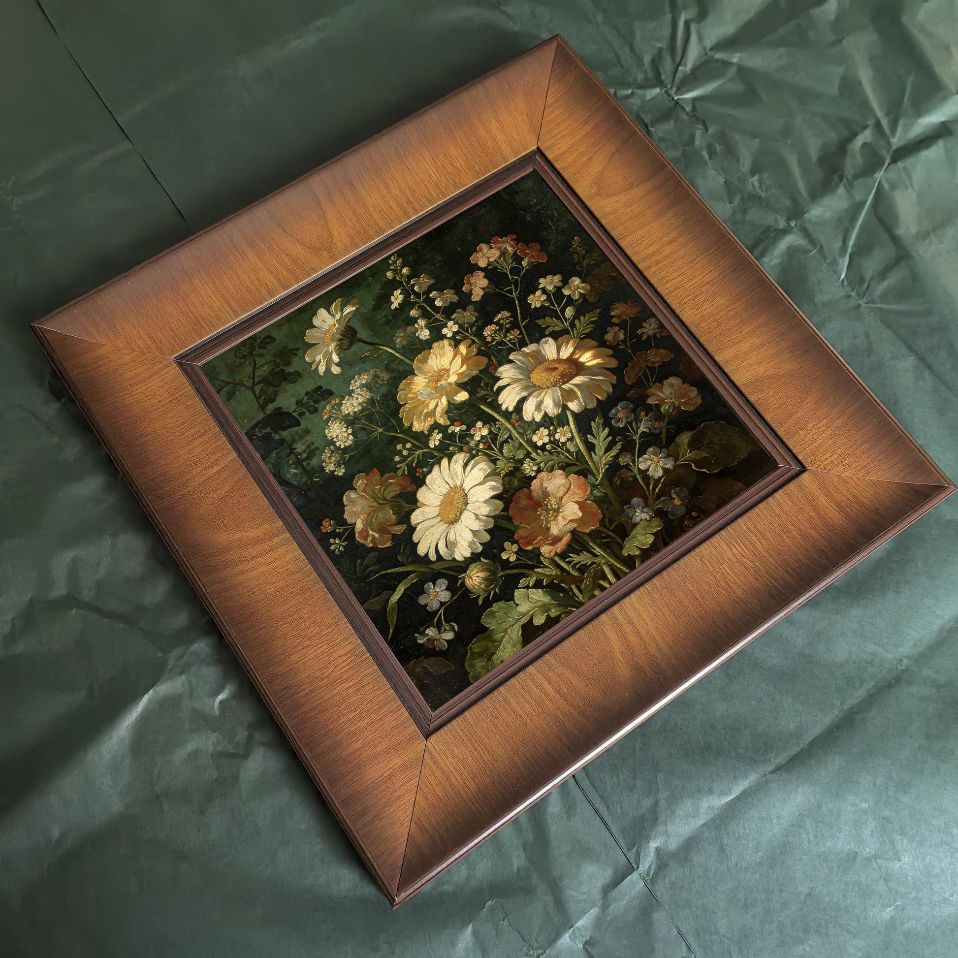 Top-down bird's-eye view of the square wooden framed painting resting on a textured green surface, highlighting the beveled edges of the frame.