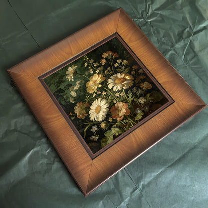 Top-down bird's-eye view of the square wooden framed painting resting on a textured green surface, highlighting the beveled edges of the frame.