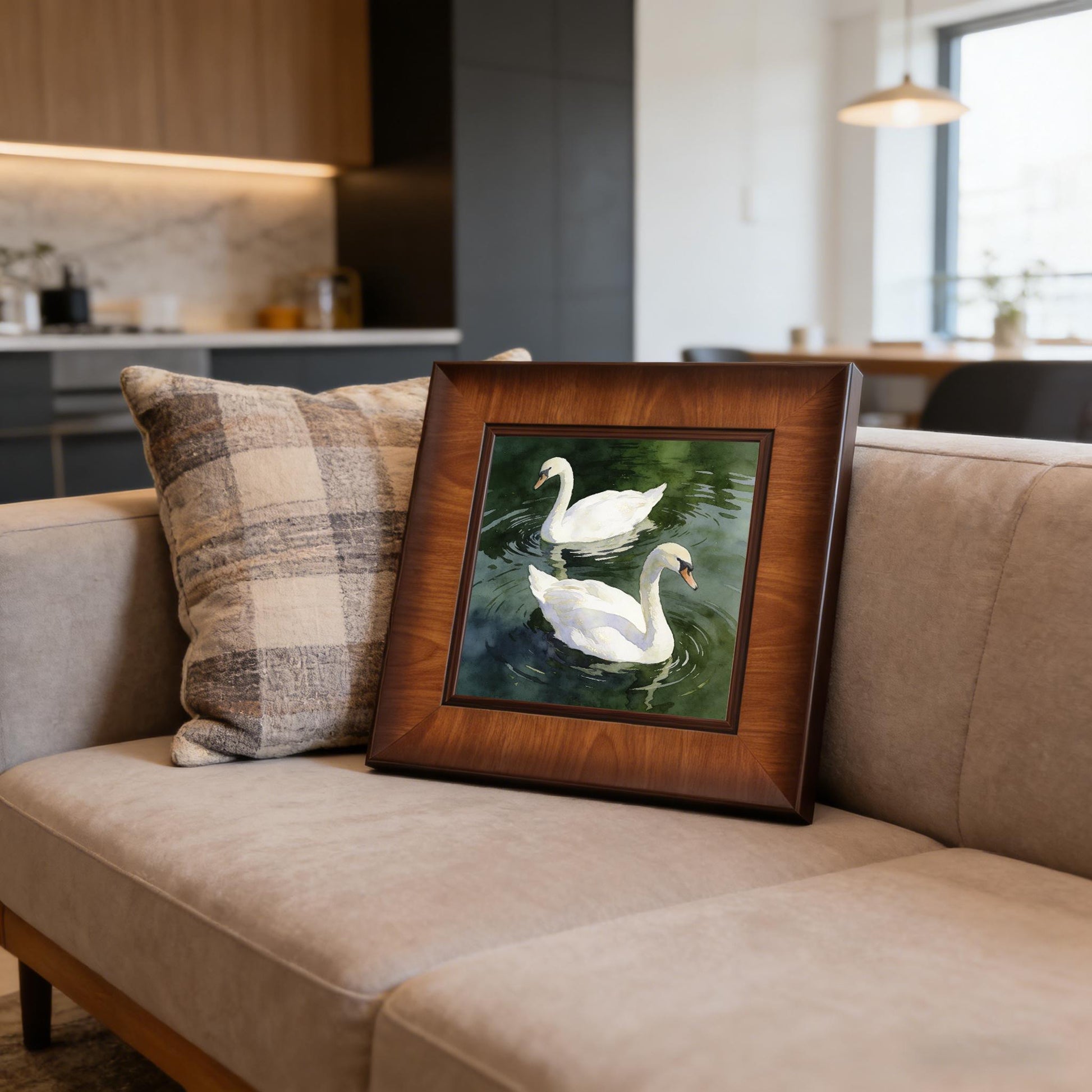 Close-up of the square swan watercolor print in a wooden frame, propped up on a light gray couch with a plaid pillow in a modern living room.