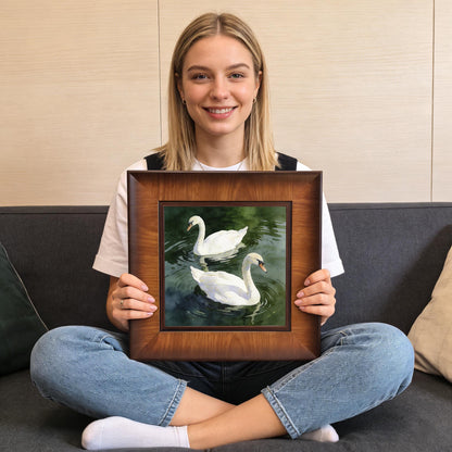 A woman sitting cross-legged on a gray sofa holding the square wood-framed swan print to show the product's scale and size.